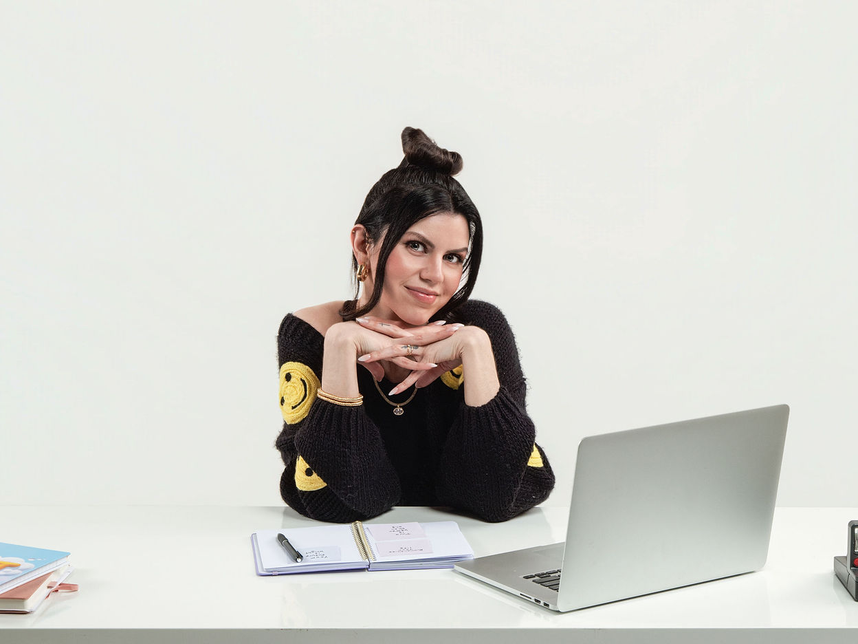 Meggan leaning on her studio desk with her chin on her hands, laptop and open notebook in front of her
